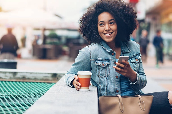young woman smiling with coffee and smart phone in hand