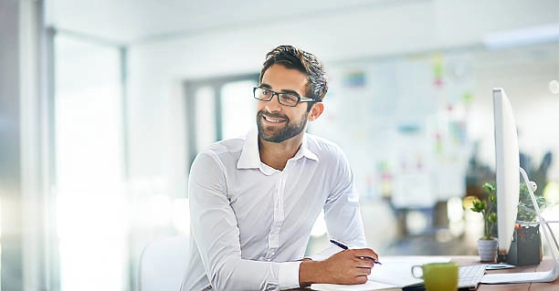 young successful man smiling at desk with pen and computer