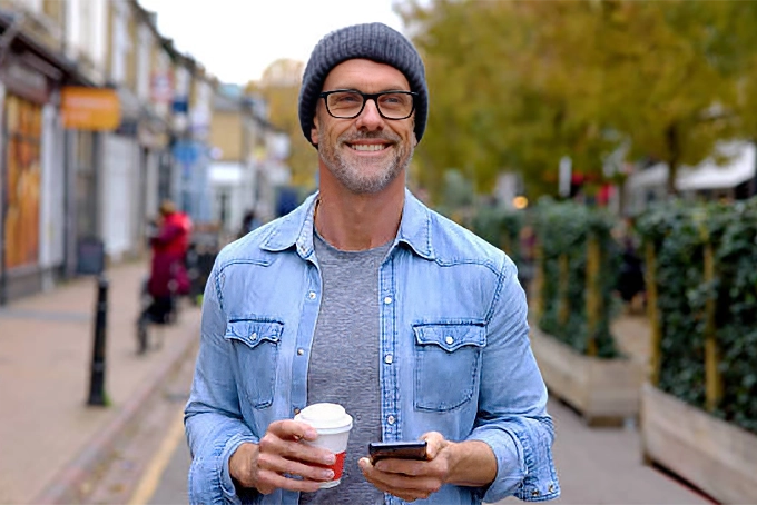 handsome middle-aged man smiling with coffee and smart phone in hand